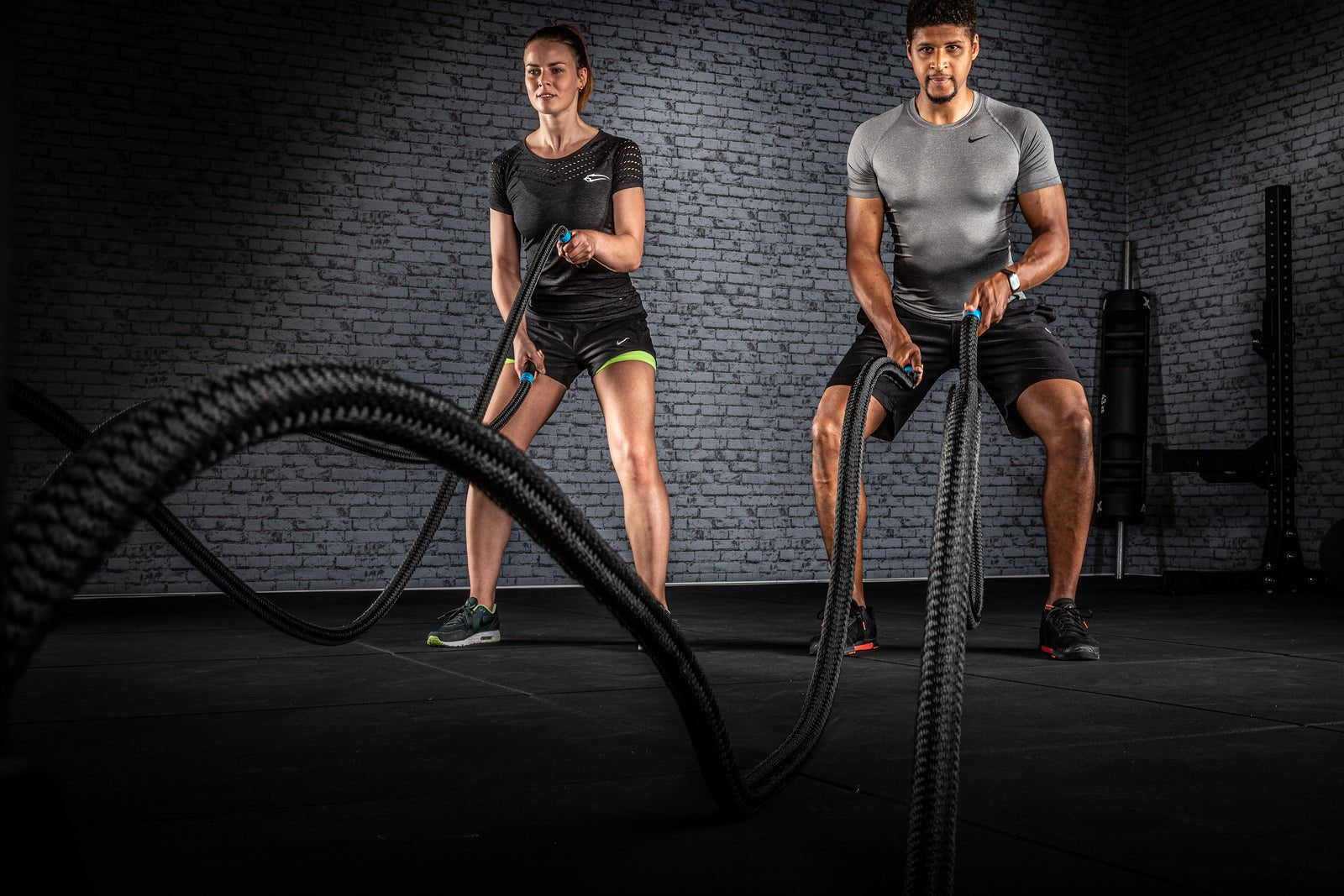 A man and a woman performing powerful battle rope waves side by side in a gym during a full-body conditioning workout