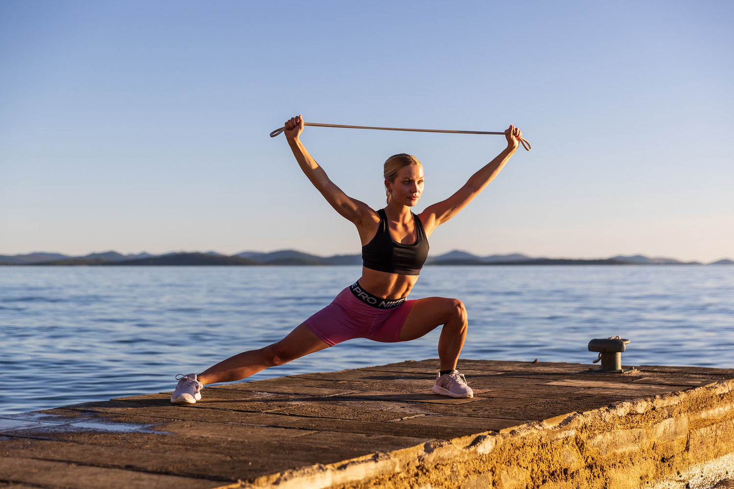 Athlete training outdoors with an aerobis Premium Powerband stretched overhead by the sea