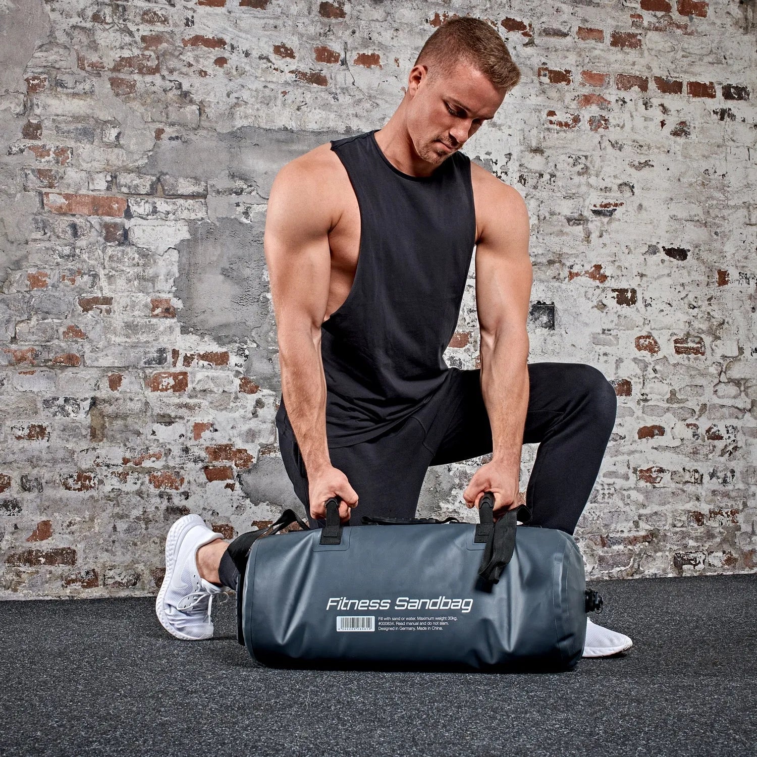 Man preparing for workout with fitness sandbag in industrial gym.