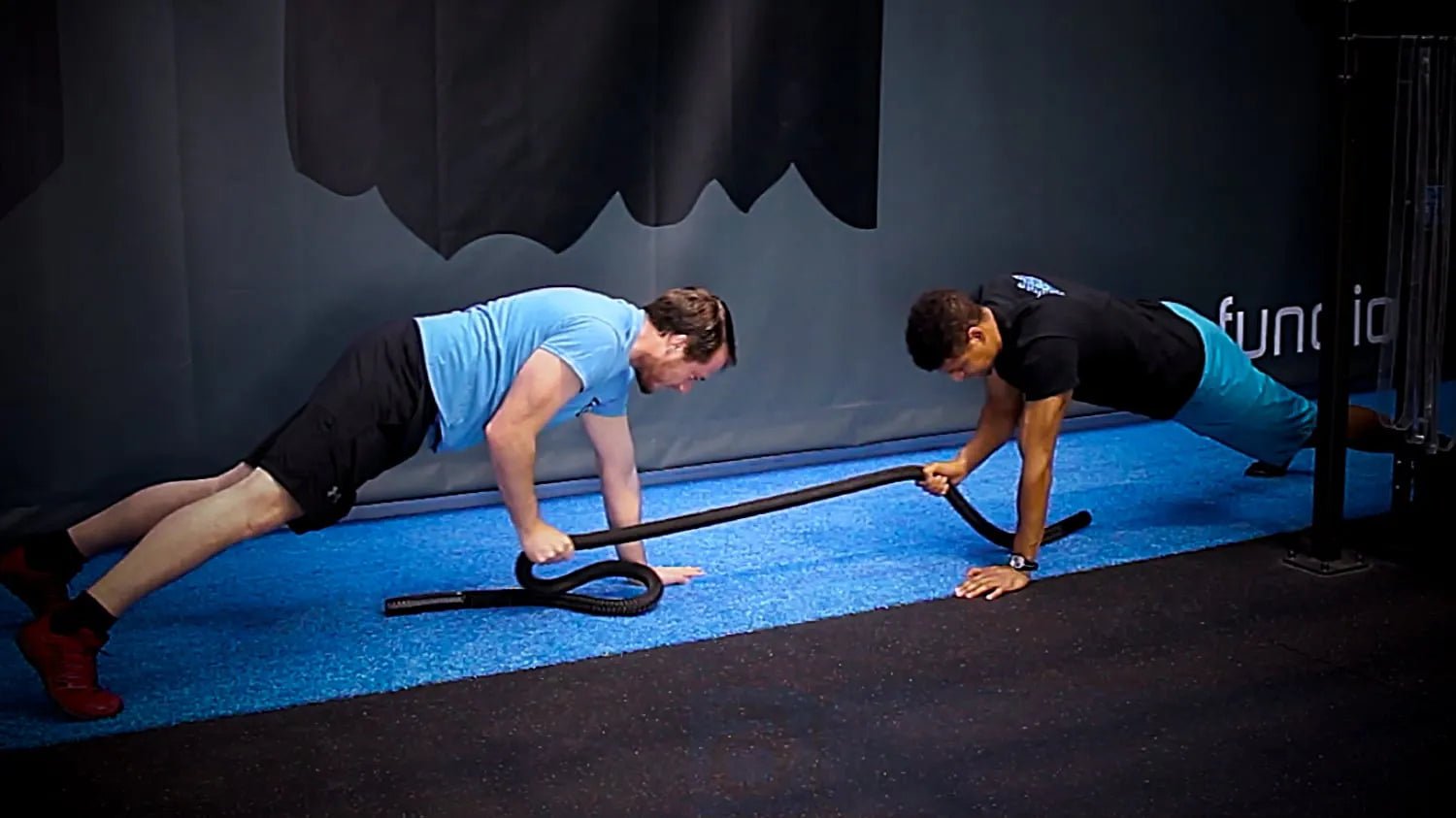 Two men performing plank exercises with a rope in a gym.