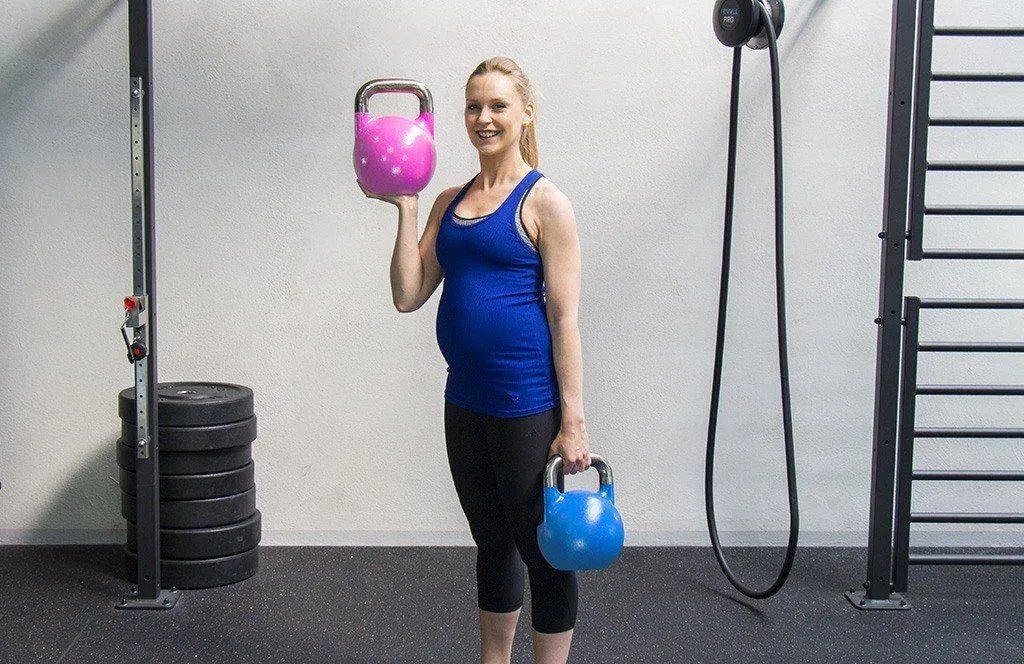 Pregnant woman training with kettlebells in a functional fitness gym.