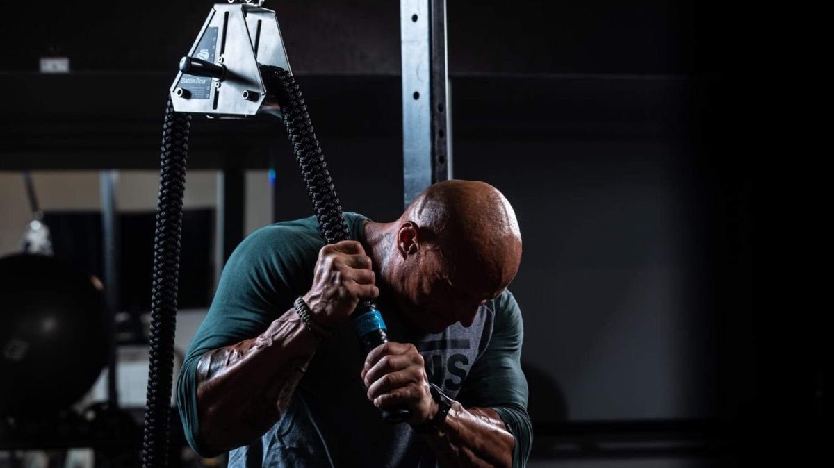 Bodybuilder using vertical rope trainer for intense arm workout.