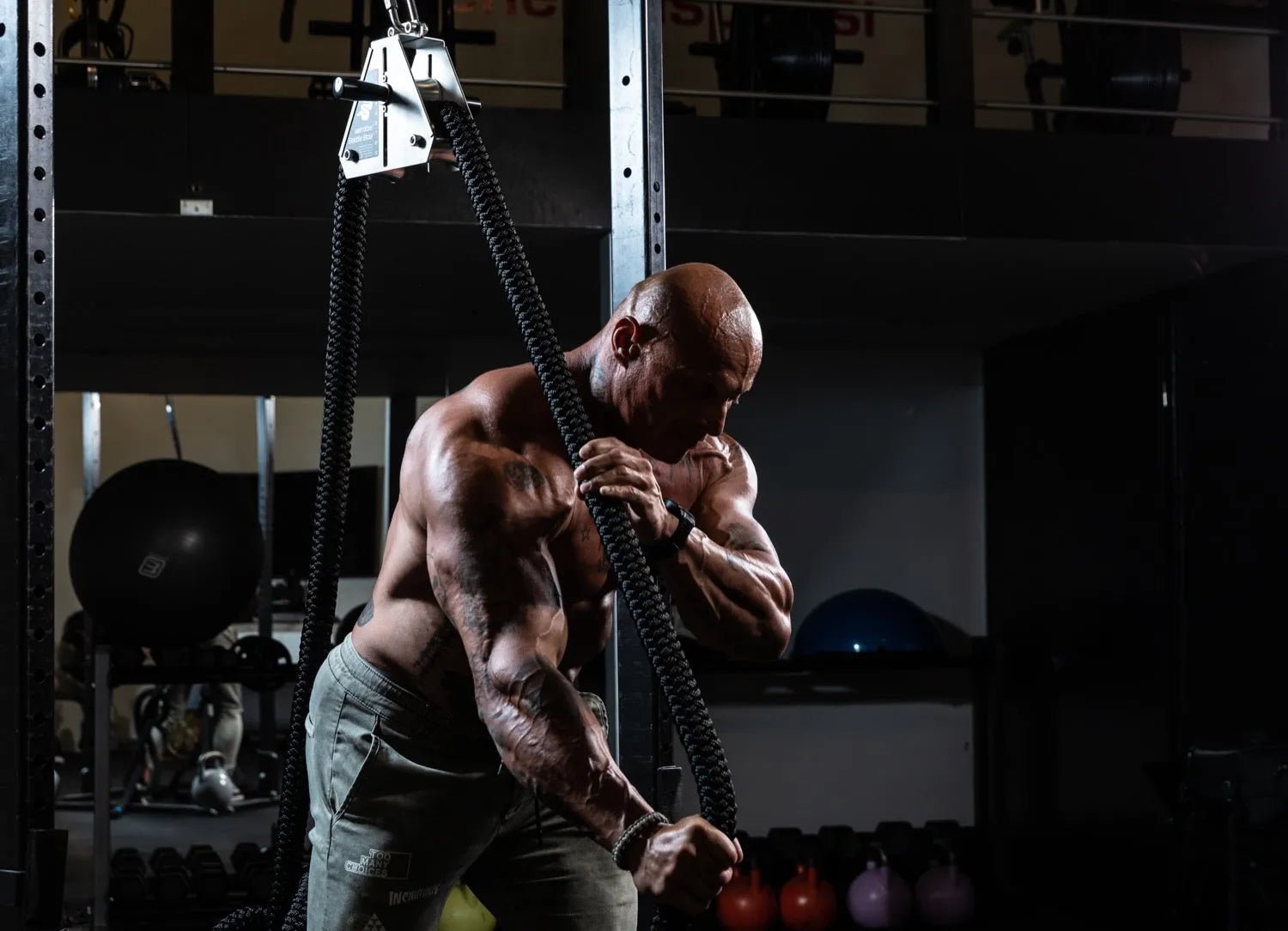 Muscular man using a rope trainer for upper body strength training.