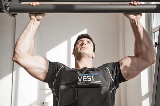 Man performing pull-ups wearing a weighted vest in a gym.