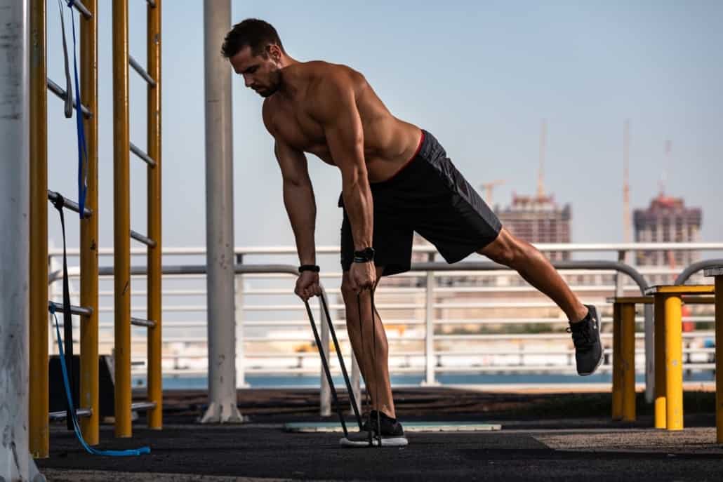 Man doing single-leg deadlifts with resistance bands outdoors.