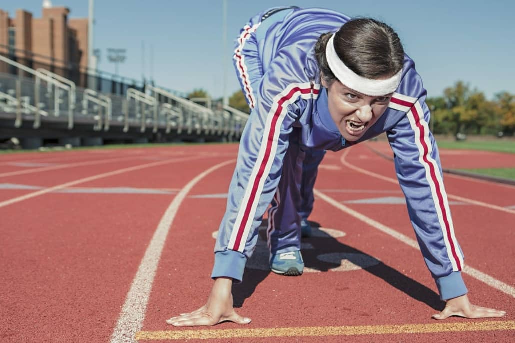 Woman in tracksuit ready to sprint on a running track.