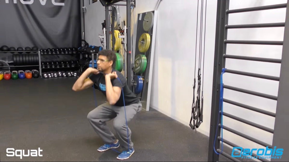 Man performing squats with resistance bands in a gym setting.