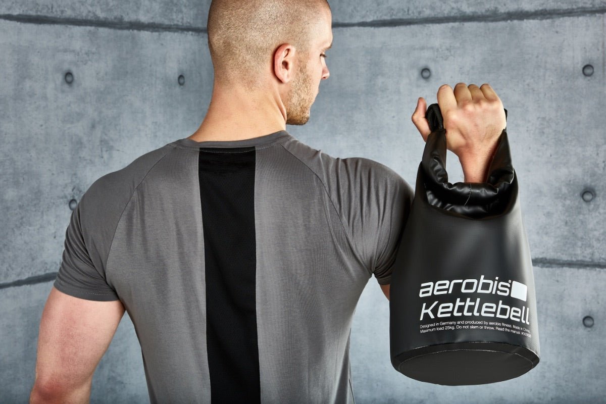 Man holding an Aerobis kettlebell on his shoulder in a gym.