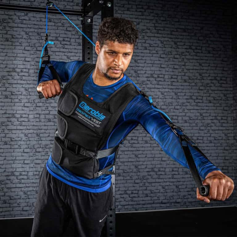 Man in a weighted vest using suspension trainers for strength.