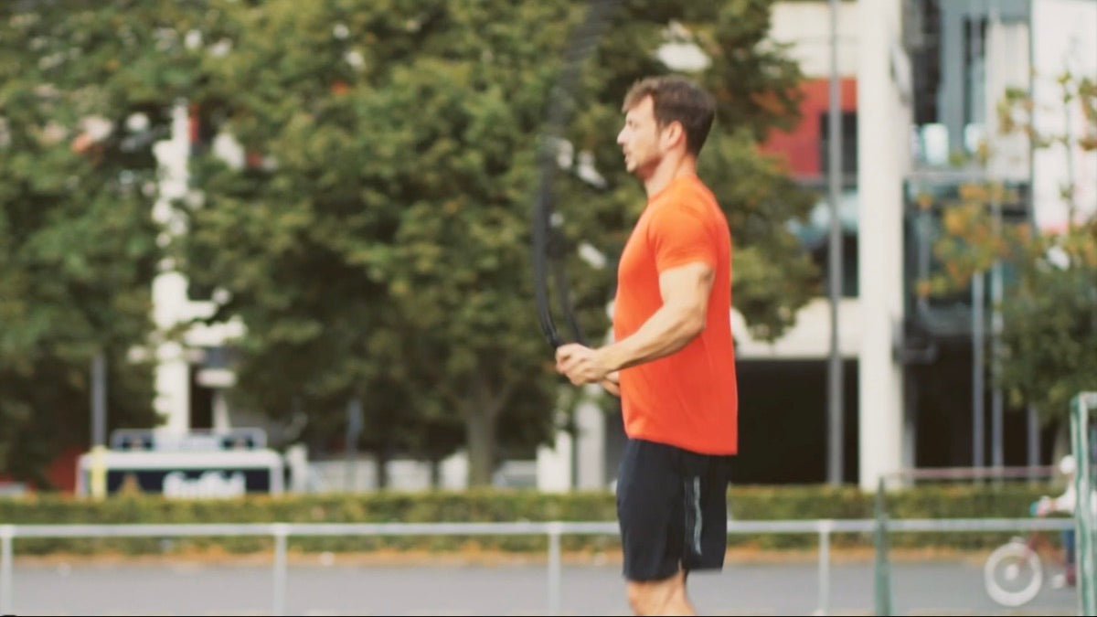 Hombre con camiseta naranja utilizando cuerdas de resistencia para entrenar al aire libre.