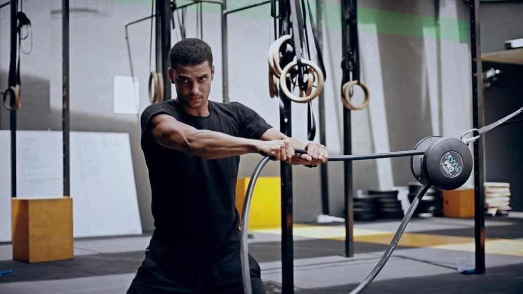 Hombre utilizando el entrenador de cuerda revvll PRO para fortalecer la parte superior del cuerpo en un gimnasio.