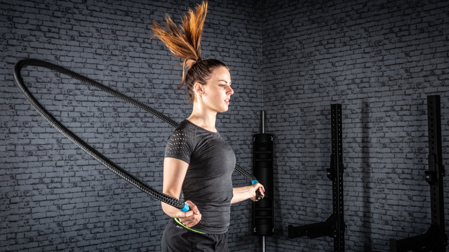 Donna che salta la corda in casa con pesanti battle ropes.