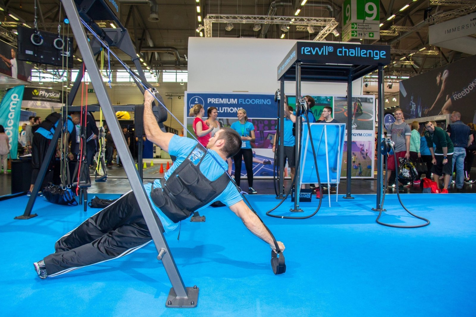 Man traint met revvll touwtrainer op fitness expo, draagt een gewichtsvest.