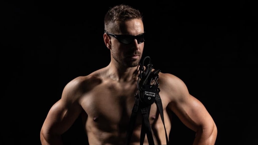 Homem com a aeroSling Tactical, a posar com equipamento de fitness.